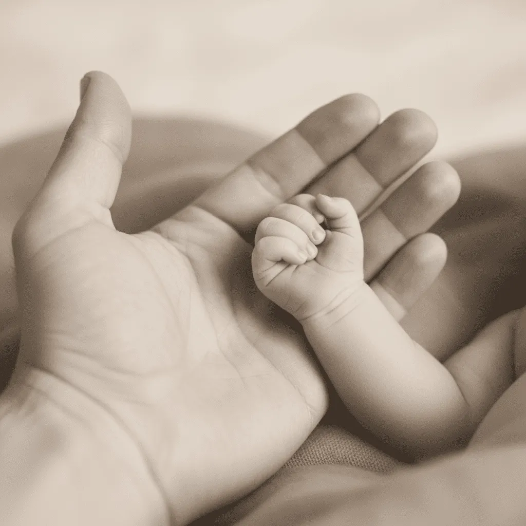 Vaters Hand mit Baby-Hand nach der Geburt – erste Berührung und Bonding