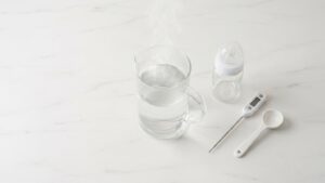 Babyflasche, Messlöffel und Wasserkanne für die hygienische Zubereitung von Pre-Nahrung auf heller Arbeitsfläche